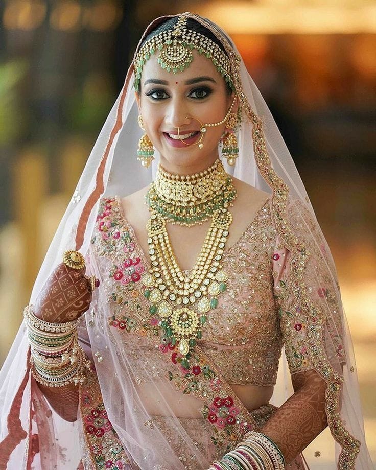 Smiling bride in a pink embroidered lehenga with gold jewellery